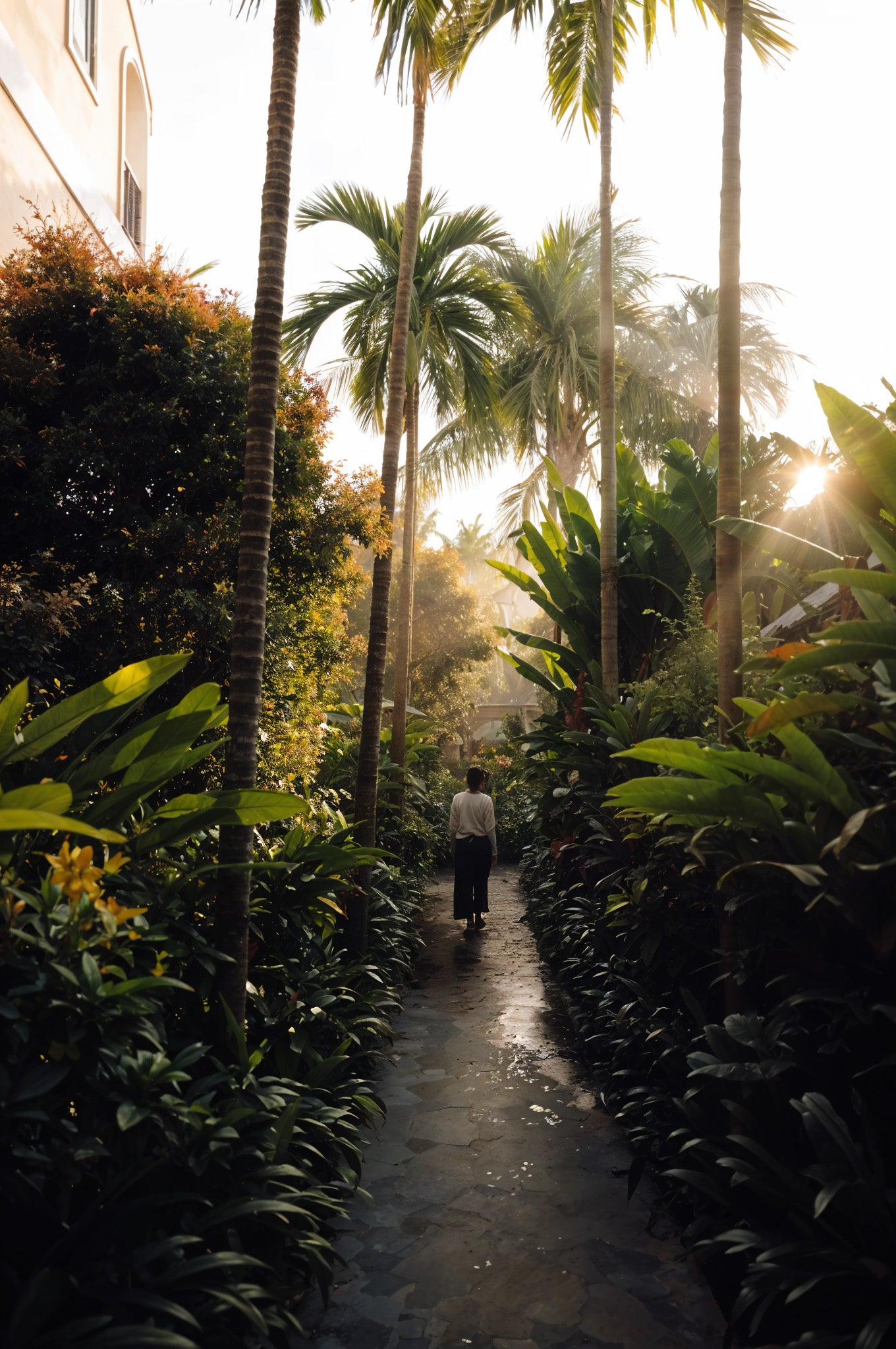 BYNOMADS Woman With Her Back Walking On A Narrow Sidewalk With Tropical Vegetation Around Her